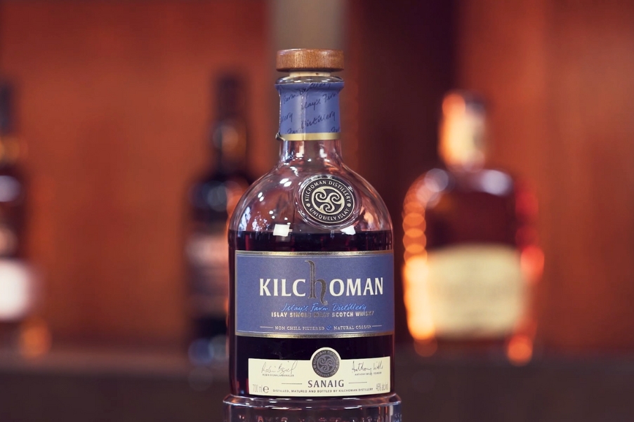 Bottle of Kilchoman Sanaig Islay Single Malt Scotch Whisky on a bar with blurred bottles in the background.